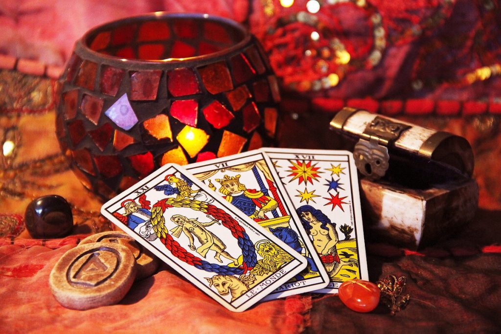 Three Marseille Tarot cards, The World, The Chariot and The Star, beside a red mosaic candle holder