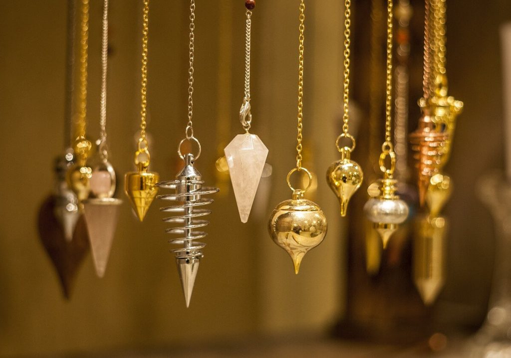 A choice of dowsing pendulums hanging on chains: gold-tone metal, silver spiral, pink crystal and copper