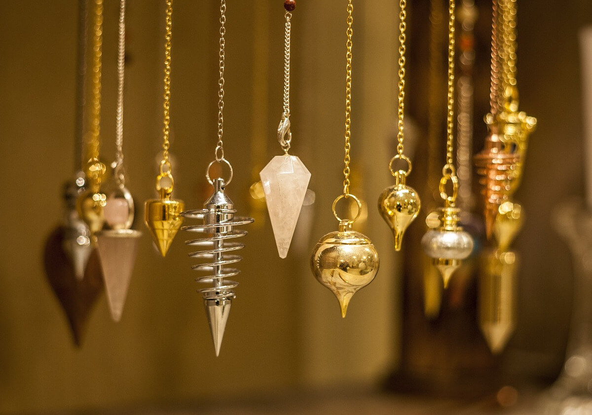 Surtido de péndulos de radiestesia colgados de cadenas: metal dorado, espiral plateada, cristal rosa y cobre