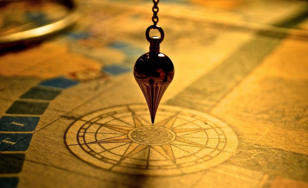 Péndulo metálico colgado de una cadena sobre la rosa de los vientos de un mapa antiguo