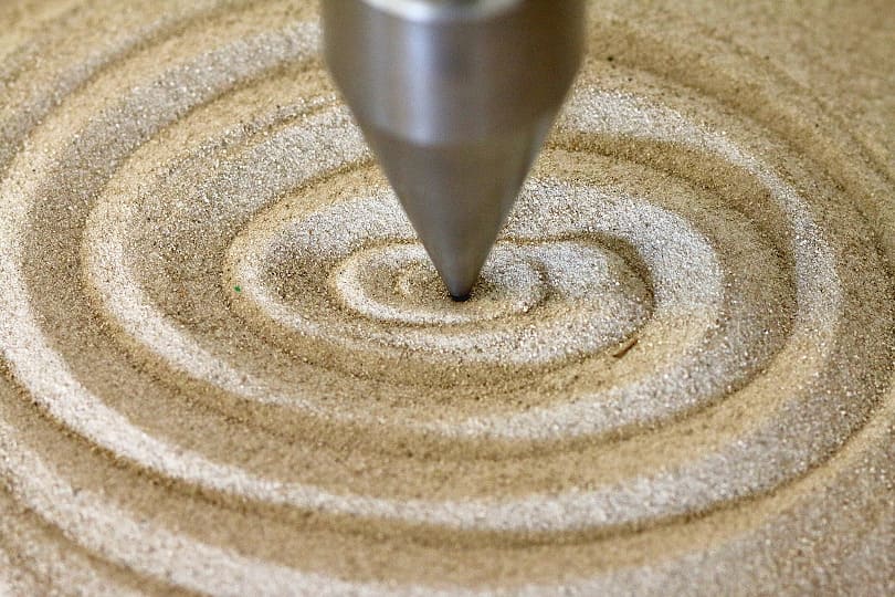 Cone-shaped metal pendulum tip tracing a spiral in fine sand