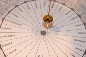 Péndulo dorado suspendido sobre una tabla circular de radiestesia con palabras numeradas en alemán