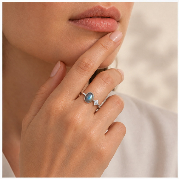 Bague toi et moi en labradorite portée au doigt, main posée contre le menton.