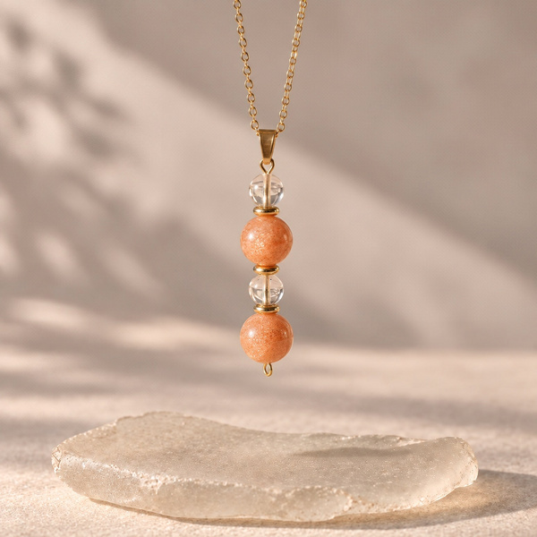 Heliodora, pendentif en pierre de soleil et cristal de roche suspendu, perles orange et transparentes l’une sous l’autre.