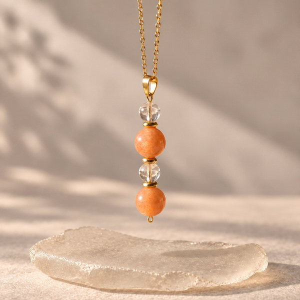 Pendentif en pierre de soleil et cristal de roche vu de plus près, sur sa chaîne dorée.