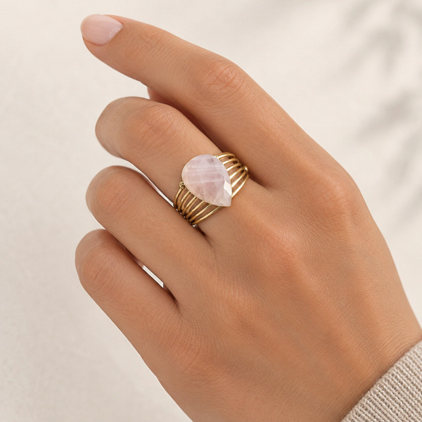 Bague ajourée en quartz rose portée au doigt, la goutte sur le dessus et les fils dorés autour.