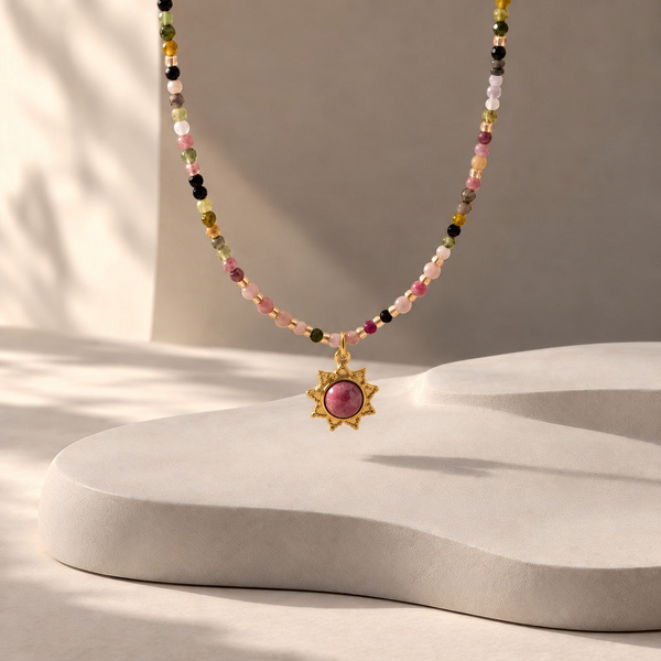 Varia, collier soleil en tourmaline multicolore suspendu, soleil doré à pierre rose sous un rang de perles colorées.