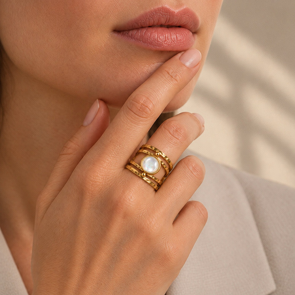 Bague martelée en nacre portée, la main relevée vers le menton.