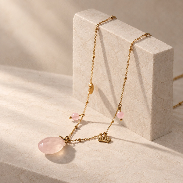 Regilla, collier couronne en quartz rose posé sur un bloc, goutte facettée, couronne dorée et perles roses.