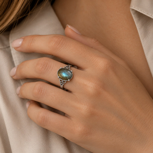 Bague ajustable en labradorite portée, la main posée sur le col d’une veste.