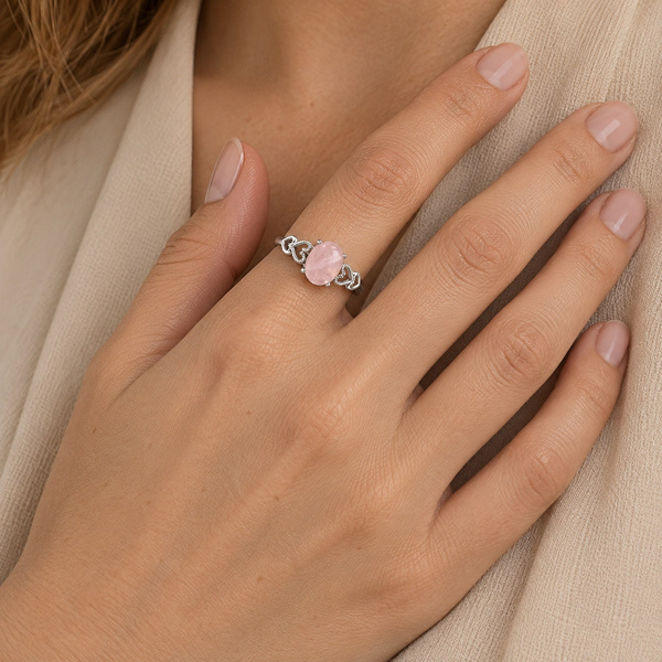 Bague cœurs en quartz rose portée, la main posée sur un tissu clair.