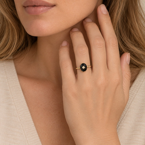 Bague étoile en agate noire portée, la main relevée près du cou.