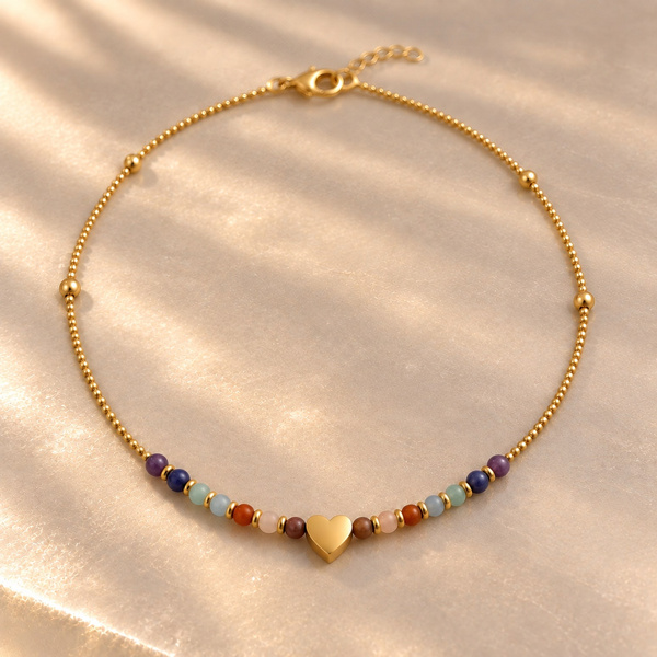 Lyde, collier cœur 7 chakras posé en cercle, perles colorées de part et d’autre d’un cœur doré.
