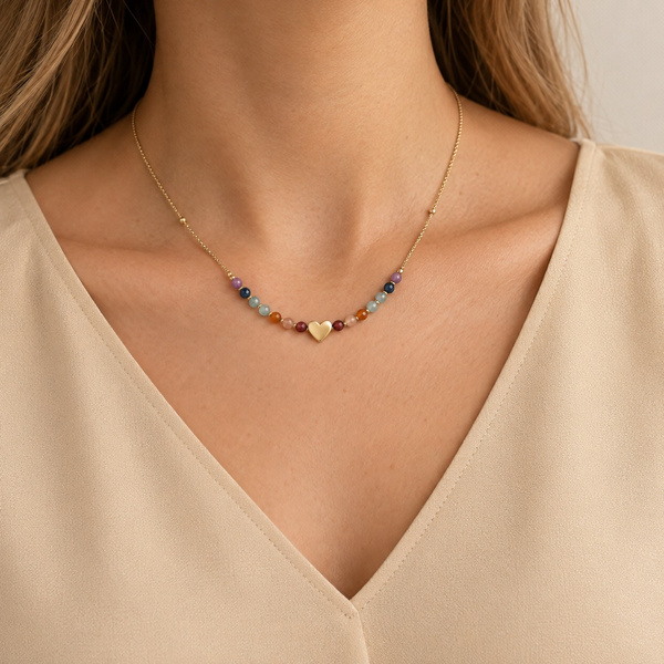Collier cœur 7 chakras porté à la base du cou, dans l’encolure d’un haut beige.